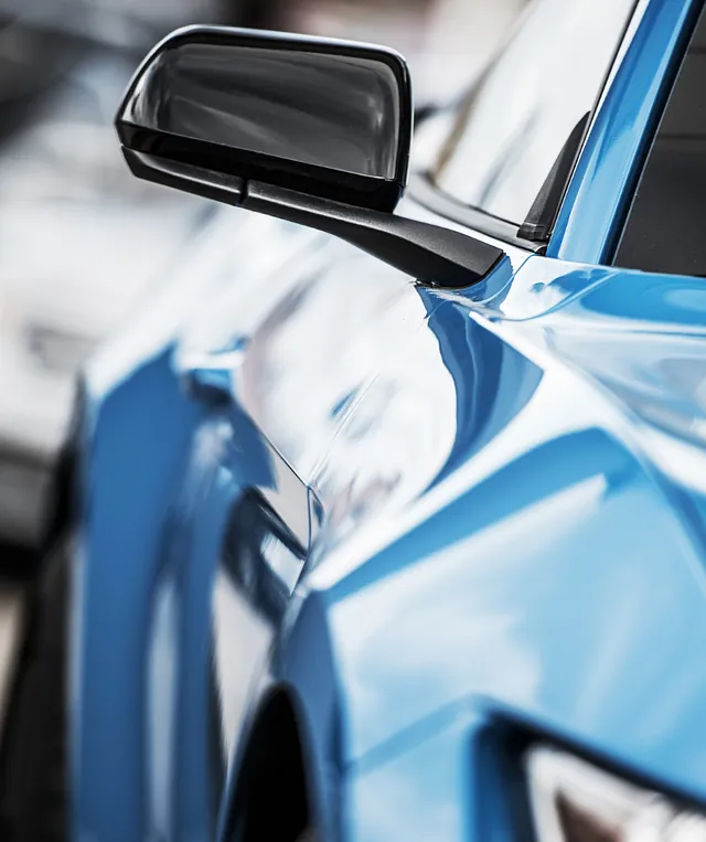 Detaljert nærbilde av sidespeilet på en blå bil, der den glansfulle lakken reflekterer omgivelsene langs bilens side.
